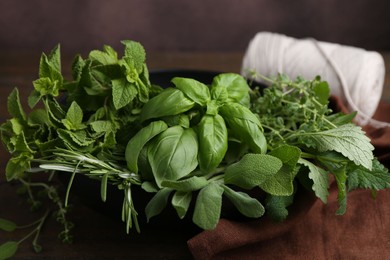 Photo of Different fresh green herbs in bowl and twine on table, closeup