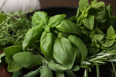 Photo of Different fresh green herbs in bowl on table, closeup