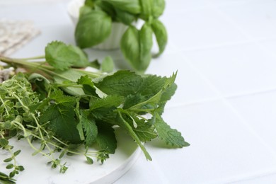 Photo of Different fresh green herbs on white tiled table, closeup. Space for text