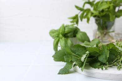 Photo of Different fresh green herbs on white tiled table, closeup. Space for text