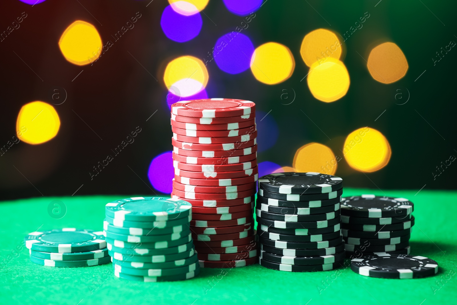Photo of Casino chips on green table against blurred lights, closeup