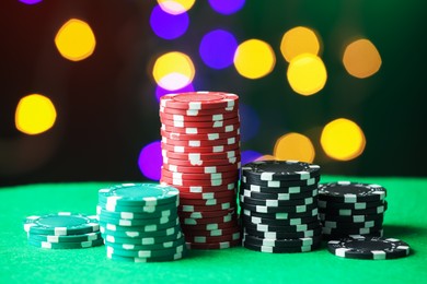 Photo of Casino chips on green table against blurred lights, closeup