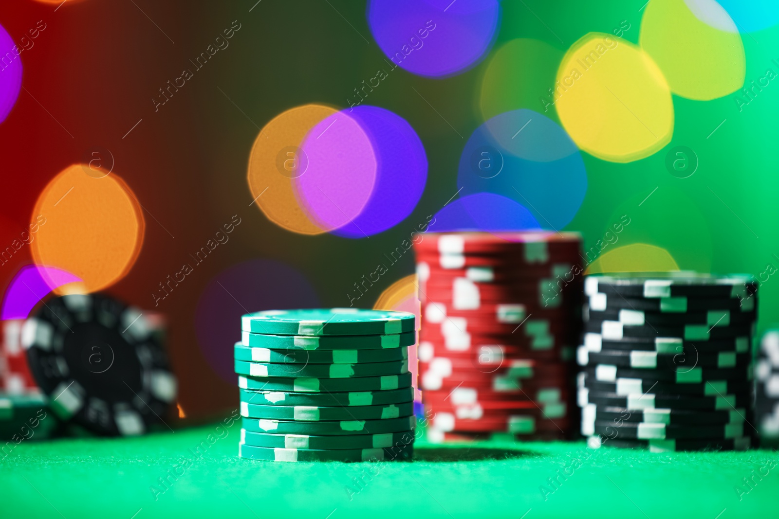 Photo of Casino chips on green table against blurred lights, closeup