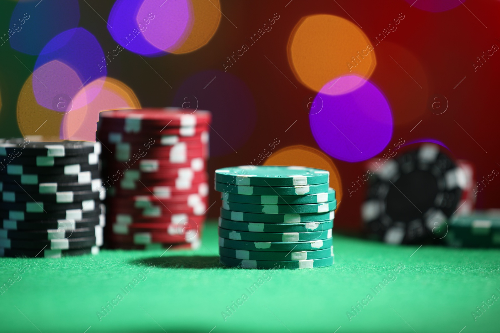 Photo of Casino chips on green table against blurred lights, closeup