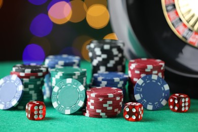 Photo of Casino chips, dice and roulette wheel on green table against blurred lights, closeup