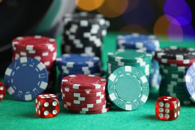 Photo of Casino chips and dice on green table against blurred lights, closeup