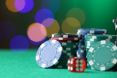 Photo of Casino chips and dice on green table against blurred lights, closeup. Space for text