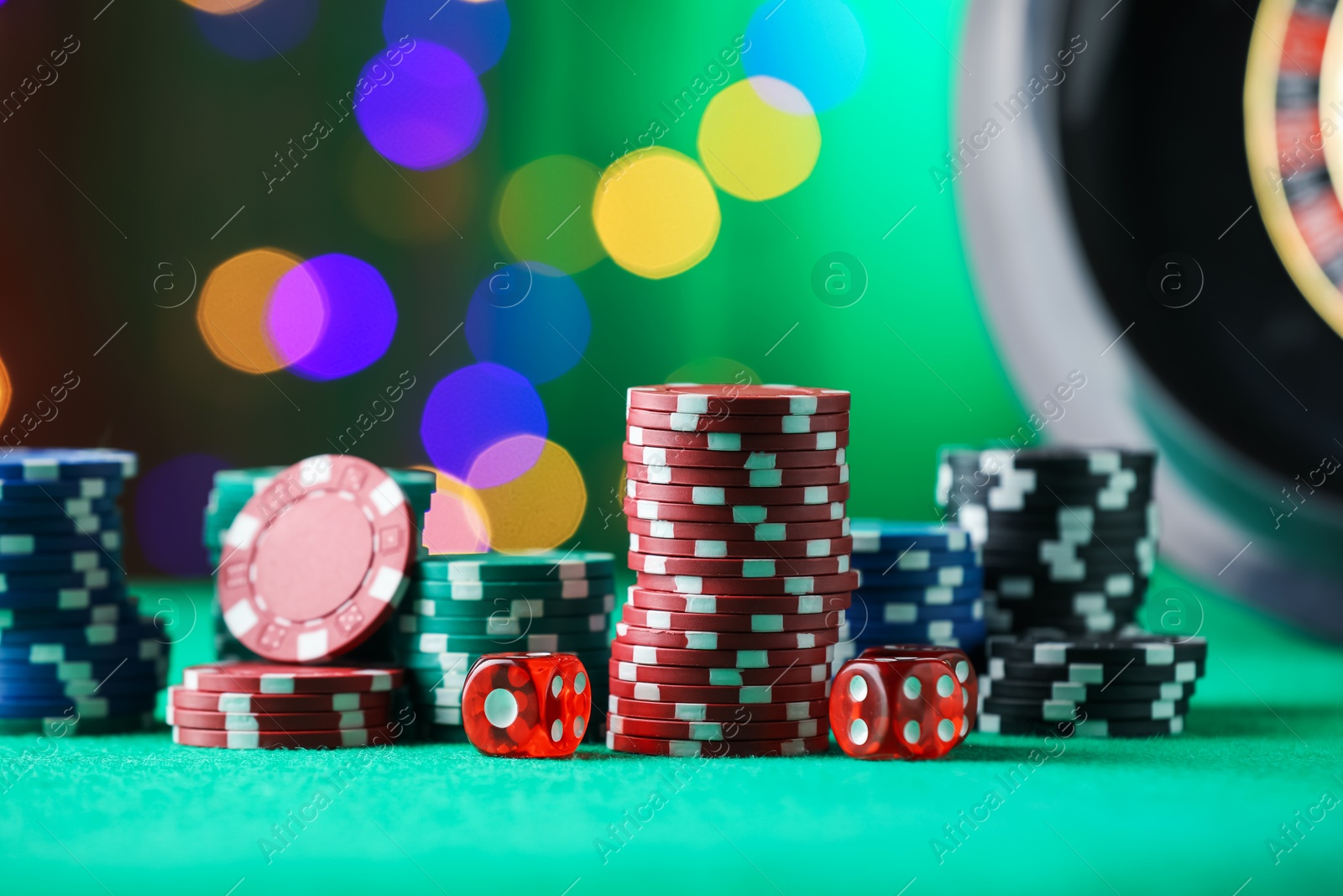 Photo of Casino chips and dice on green table against blurred lights, closeup