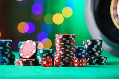 Photo of Casino chips and dice on green table against blurred lights, closeup