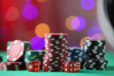 Photo of Casino chips and dice on green table against blurred lights, closeup