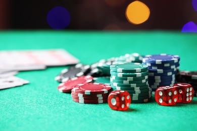 Photo of Casino chips and dice on green table against blurred lights, closeup. Space for text