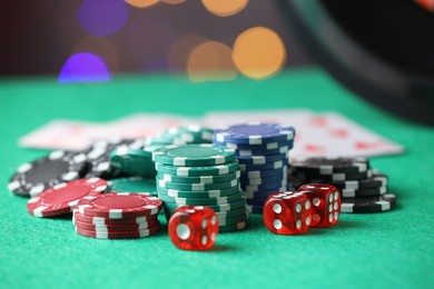 Photo of Casino chips and dice on green table against blurred lights, closeup