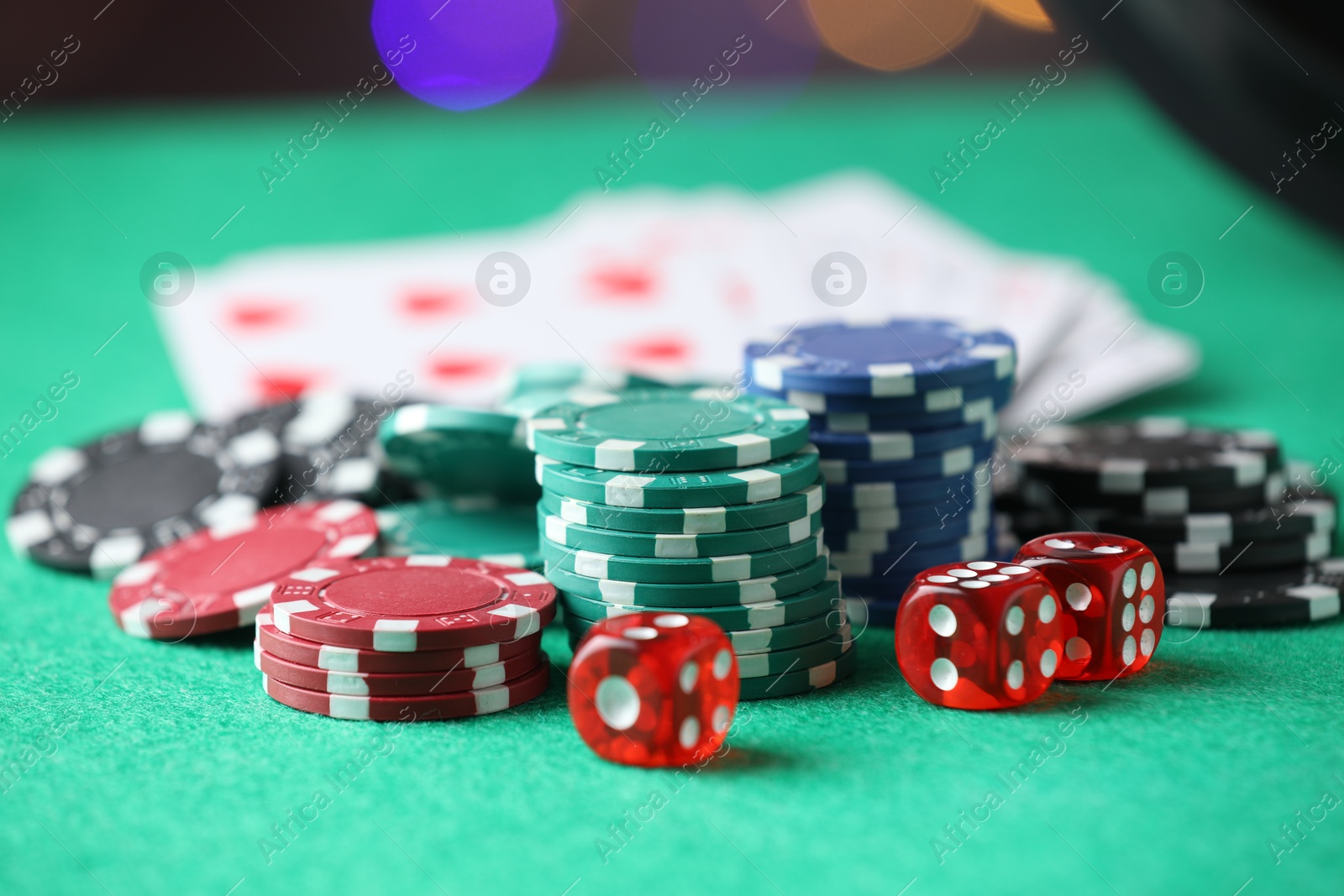 Photo of Casino chips, dice and playing cards on green table against blurred lights, closeup