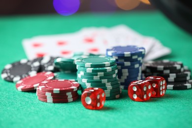 Photo of Casino chips, dice and playing cards on green table against blurred lights, closeup