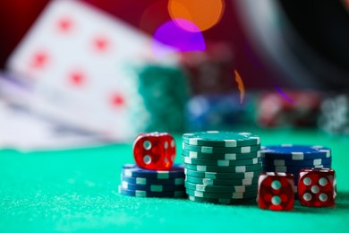 Photo of Casino chips and dice on green table against blurred lights, closeup. Space for text