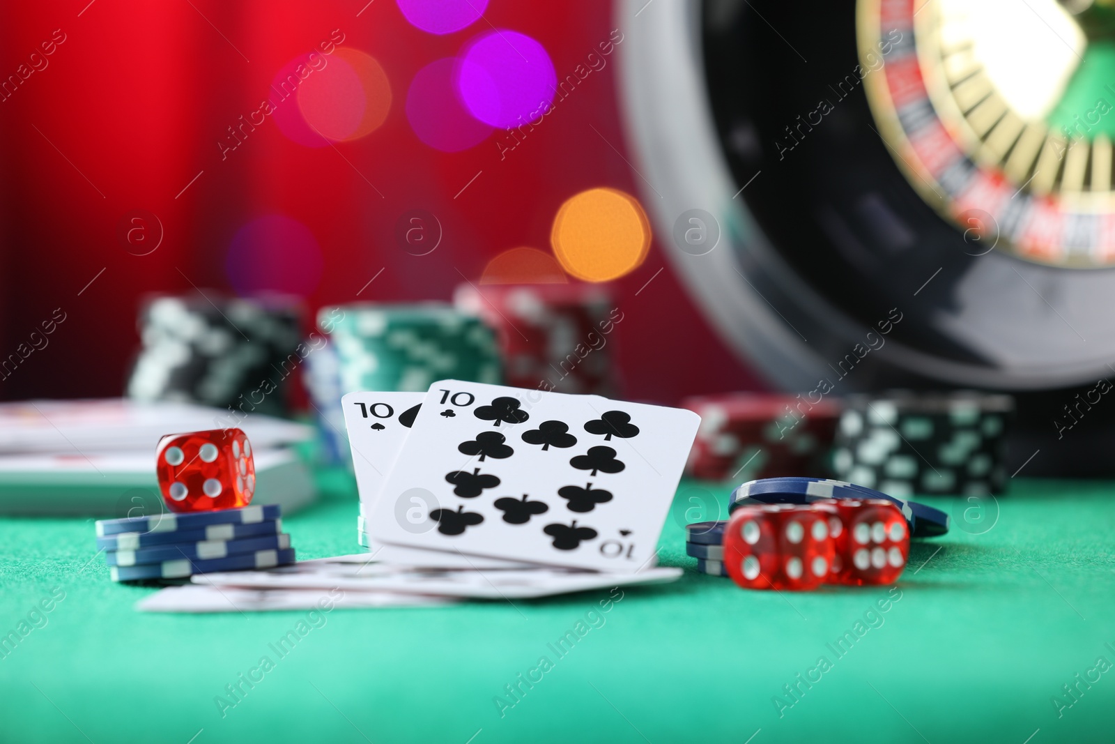 Photo of Casino chips, dice and playing cards on green table against blurred lights, closeup