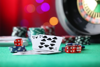 Photo of Casino chips, dice and playing cards on green table against blurred lights, closeup