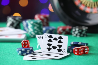Photo of Casino chips, dice and playing cards on green table against blurred lights, closeup