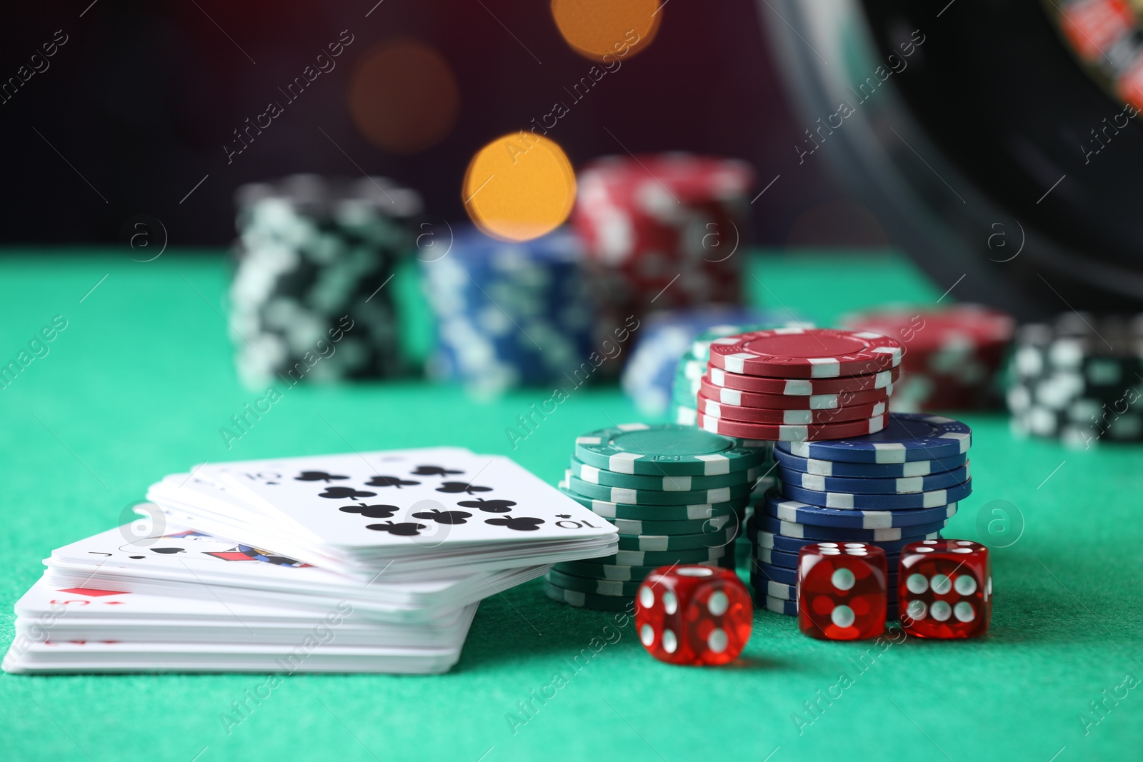 Photo of Casino chips, dice and playing cards on green table against blurred lights, closeup