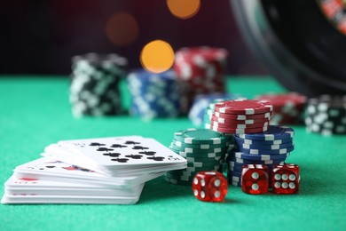 Photo of Casino chips, dice and playing cards on green table against blurred lights, closeup