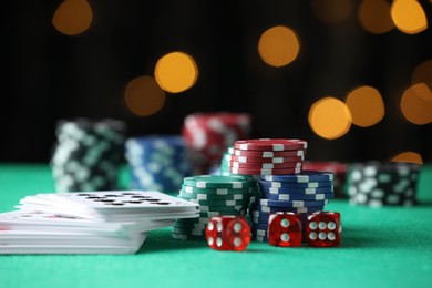 Photo of Casino chips, dice and playing cards on green table against blurred lights, closeup