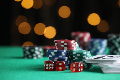 Photo of Casino chips, dice and playing cards on green table against blurred lights, closeup