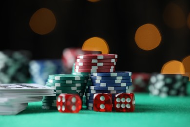Photo of Casino chips, dice and playing cards on green table against blurred lights, closeup