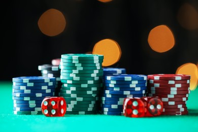 Photo of Casino chips and dice on green table against blurred lights, closeup
