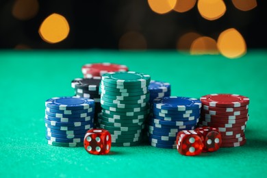 Photo of Casino chips and dice on green table against blurred lights, closeup