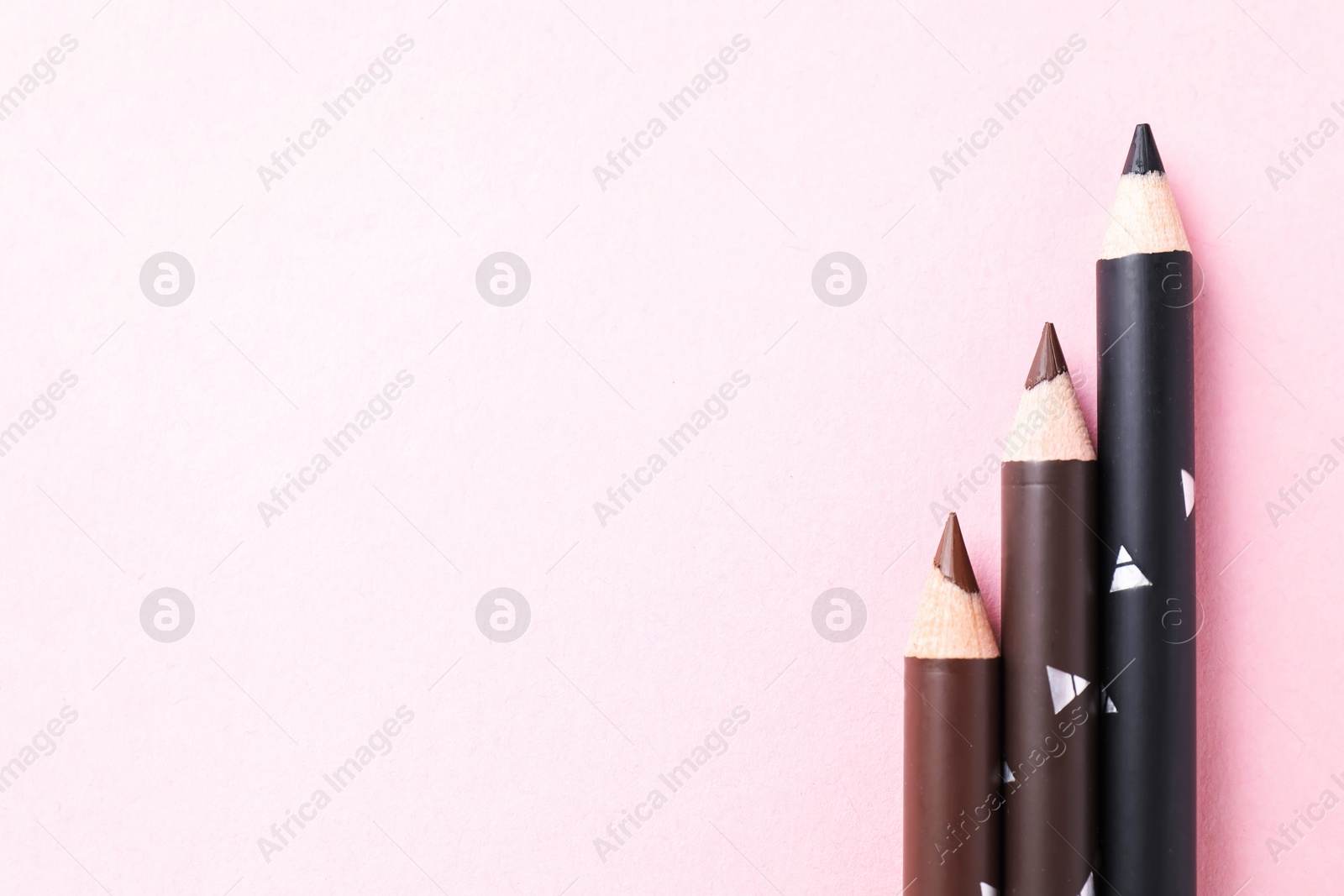 Different eyebrow pencils on pink background, flat lay. Space for text Photo of Different eyebrow pencils on pink background, flat lay. Space for text