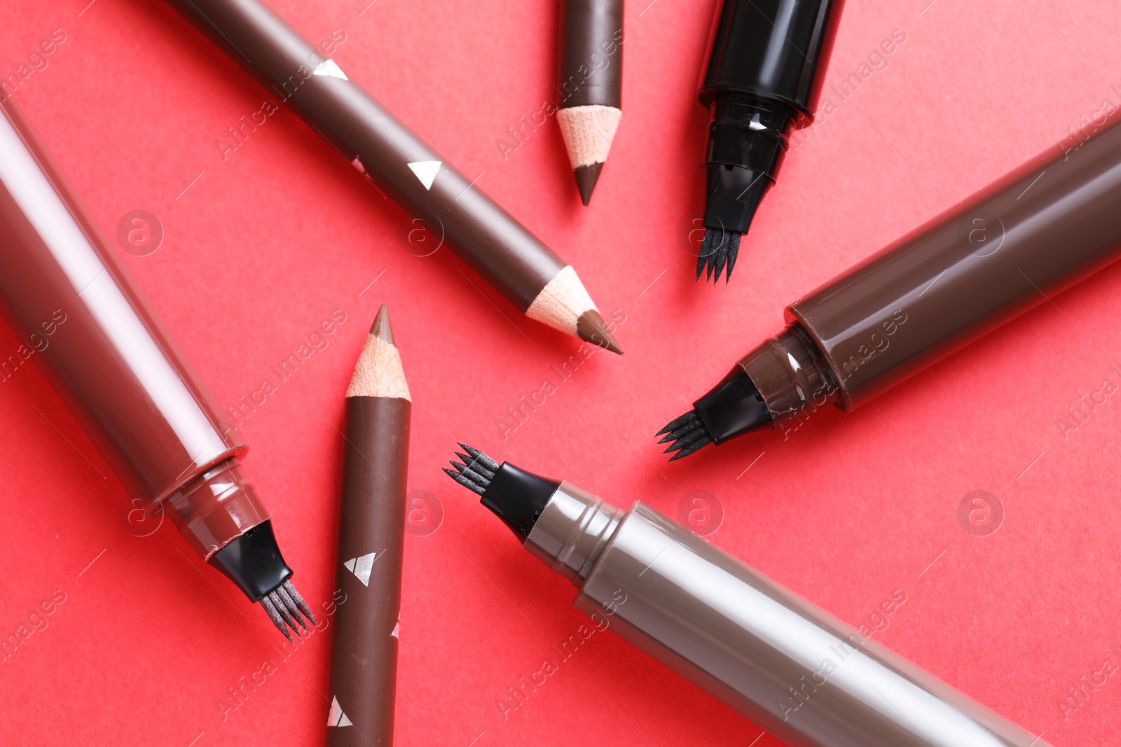 Different eyebrow pencils on red background, flat lay Photo of Different eyebrow pencils on red background, flat lay