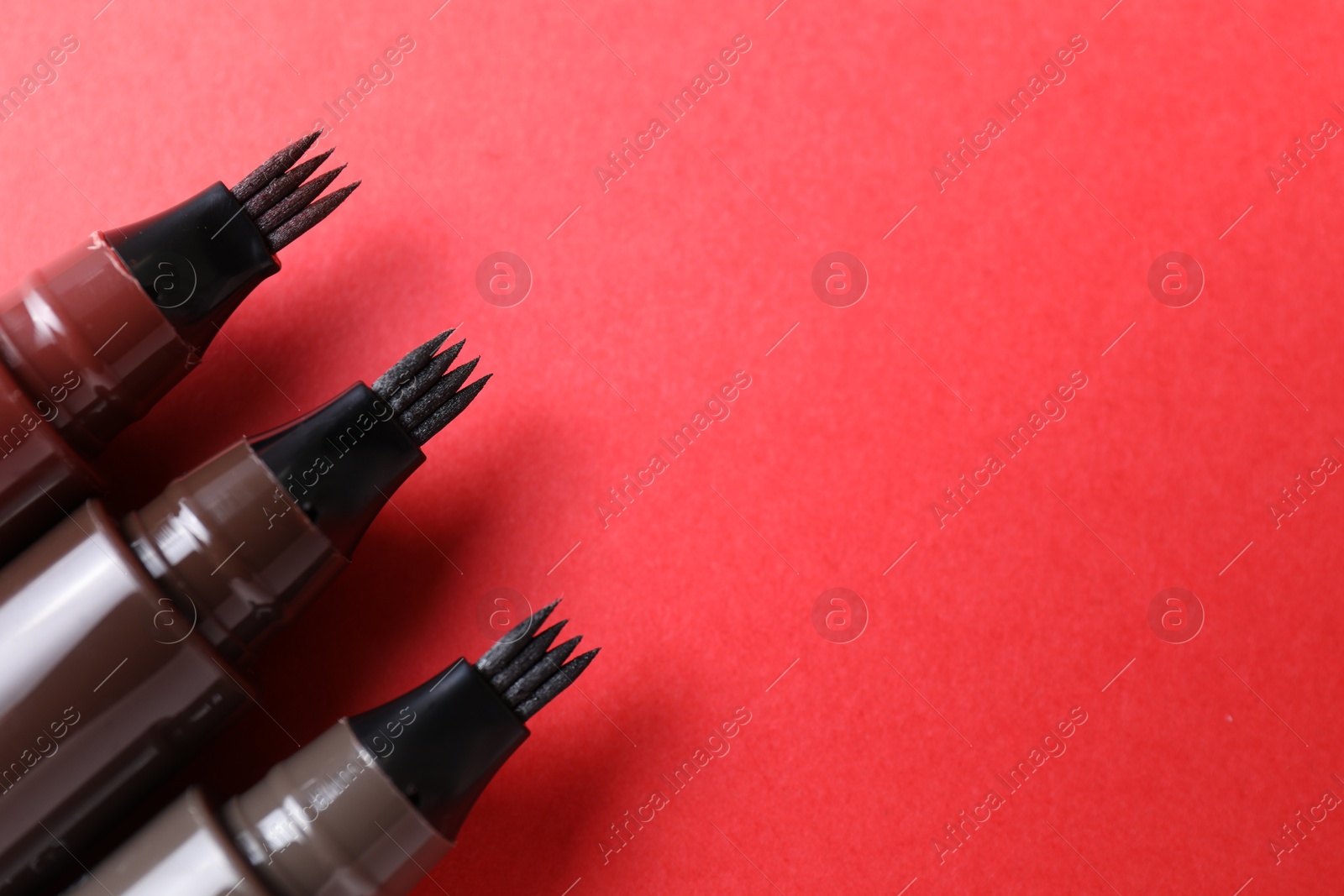 Liquid eyebrow pencils on red background, above view. Space for text Photo of Liquid eyebrow pencils on red background, above view. Space for text