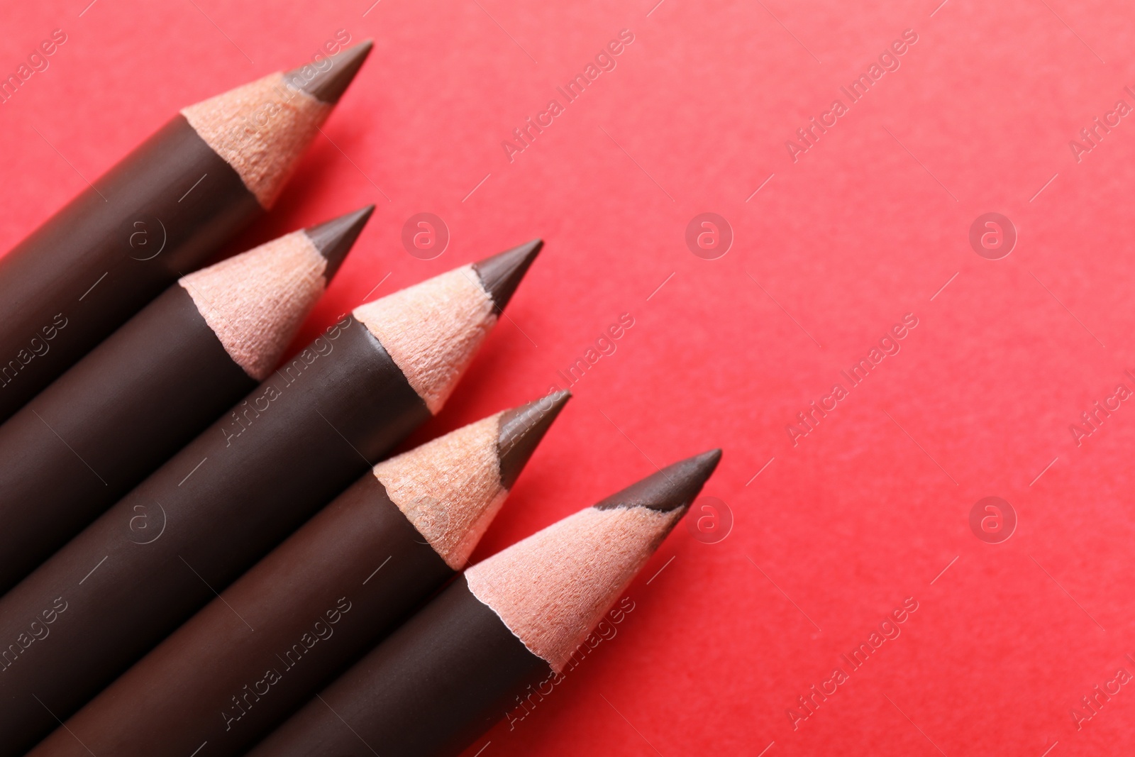 Many eyebrow pencils on red background, above view. Space for text Photo of Many eyebrow pencils on red background, above view. Space for text