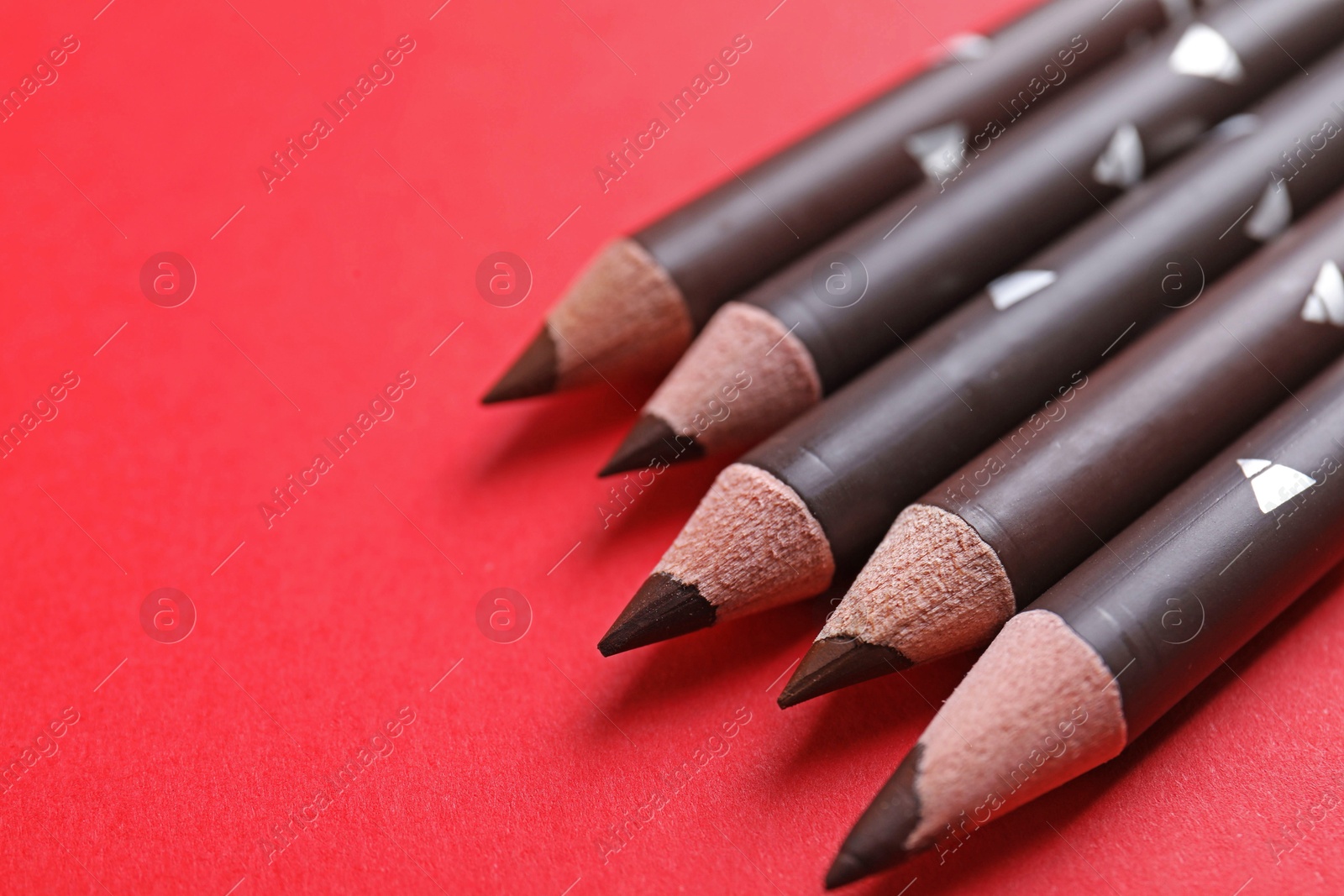 Many eyebrow pencils on red background, closeup. Space for text Photo of Many eyebrow pencils on red background, closeup. Space for text