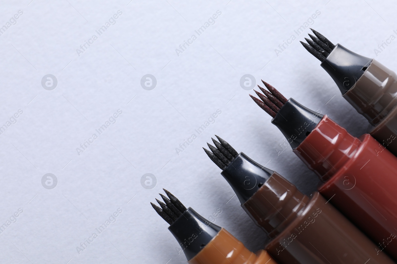 Liquid eyebrow pencils on white background, flat lay. Space for text Photo of Liquid eyebrow pencils on white background, flat lay. Space for text