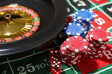 Photo of Casino chips, dice and roulette wheel on table, closeup