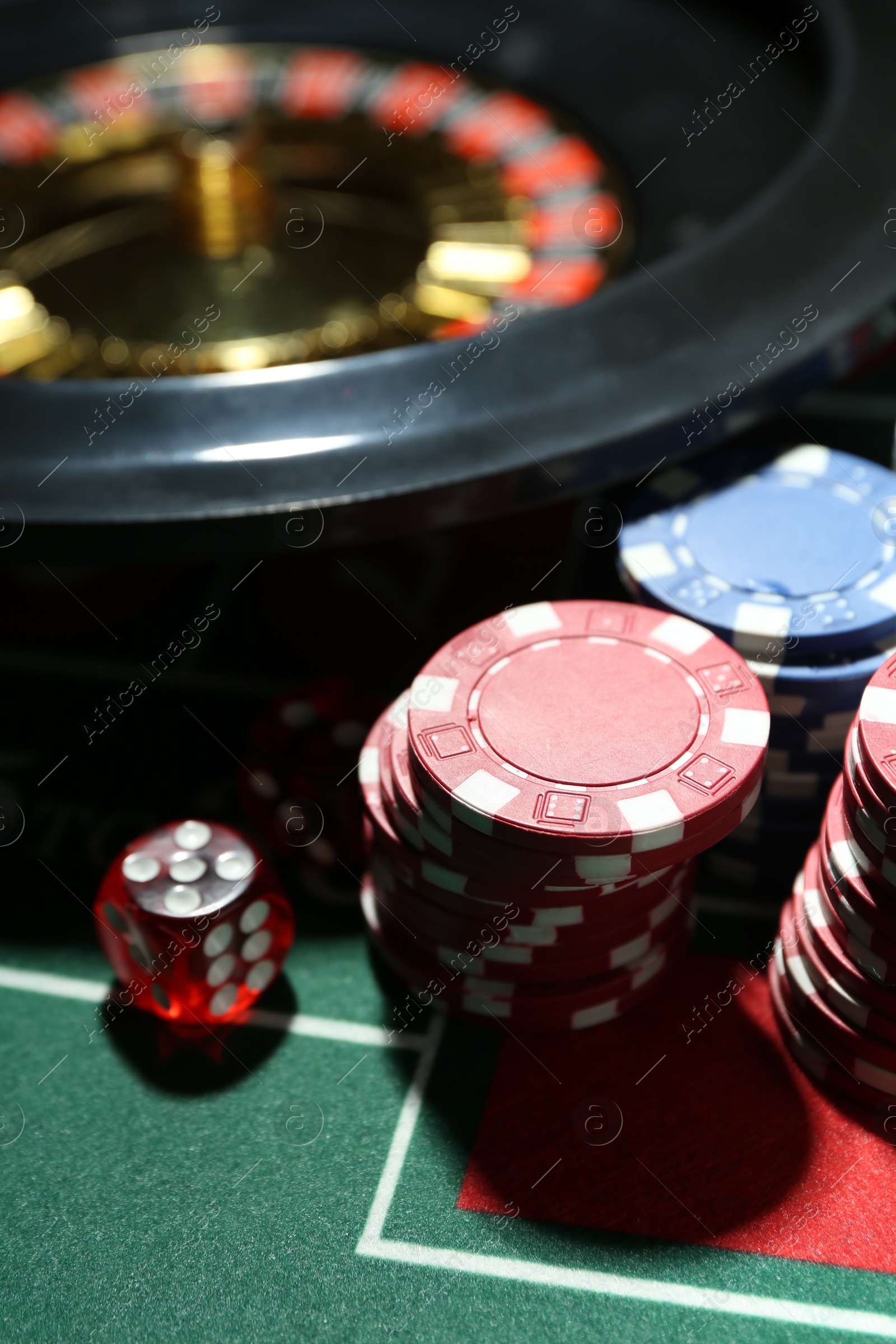 Photo of Casino chips, die and roulette wheel on table, closeup