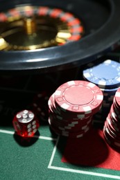 Photo of Casino chips, die and roulette wheel on table, closeup