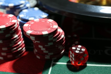 Photo of Casino chips, die and roulette wheel on table, closeup