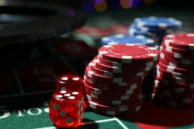 Photo of Casino chips and dice on roulette table against blurred lights, closeup