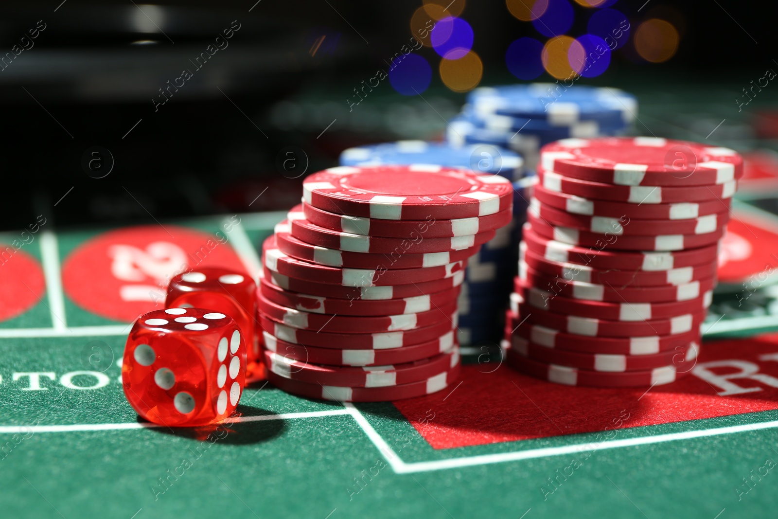 Photo of Casino chips and dice on roulette table against blurred lights, closeup