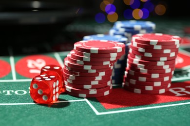Photo of Casino chips and dice on roulette table against blurred lights, closeup