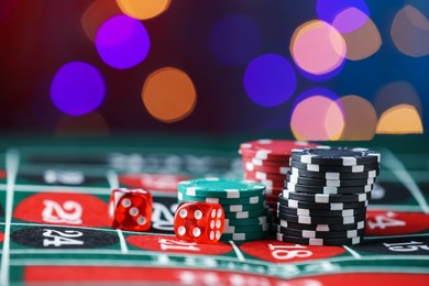 Photo of Casino chips and dice on roulette table against blurred lights, closeup