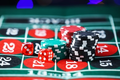 Photo of Casino chips and dice on roulette table against blurred lights, closeup