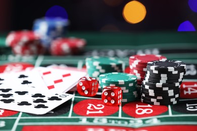 Photo of Casino chips, dice and playing cards on roulette table against blurred lights, closeup