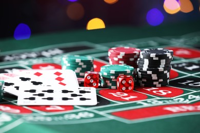 Photo of Casino chips, dice and playing cards on roulette table against blurred lights, closeup