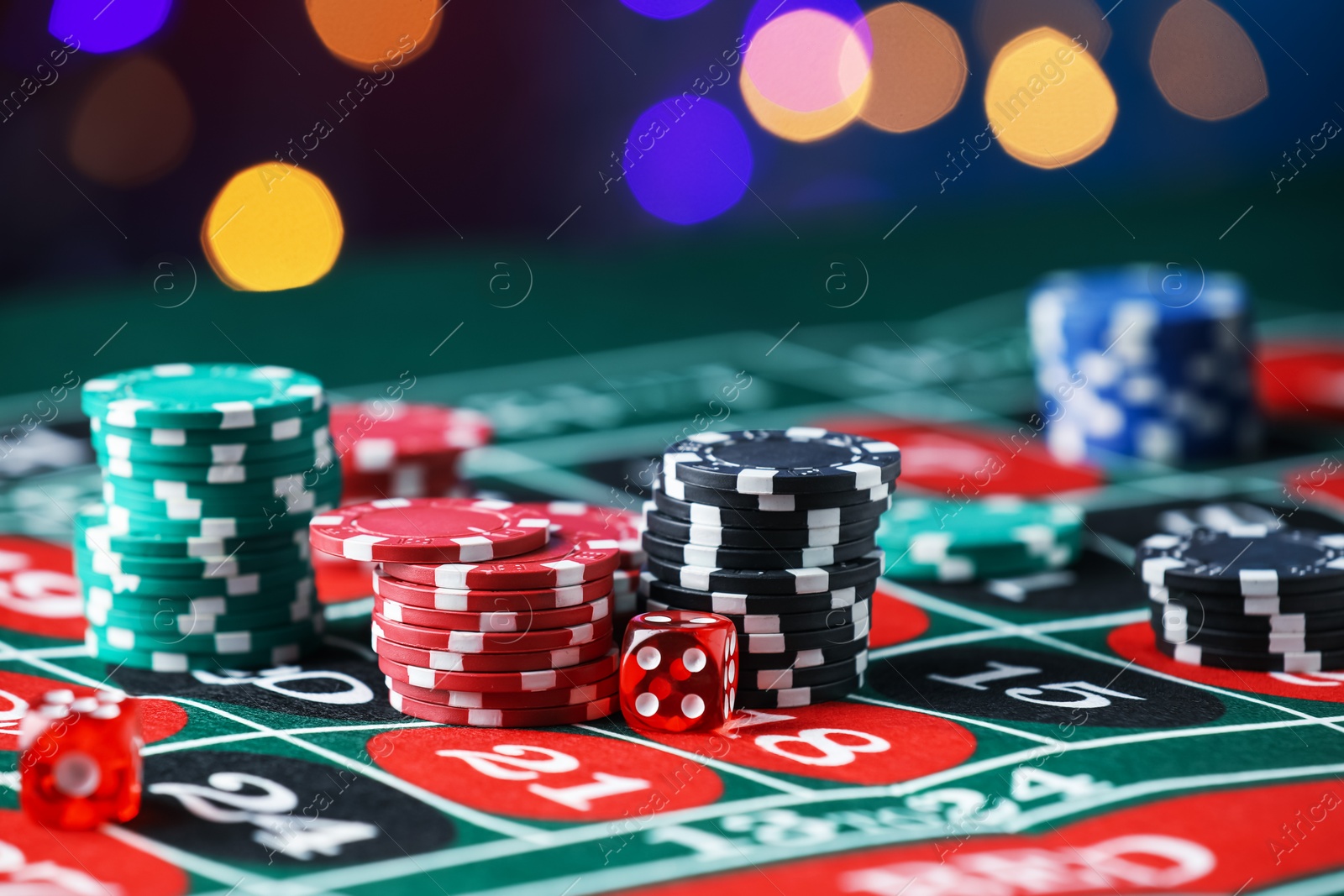 Photo of Casino chips and dice on roulette table against blurred lights, closeup