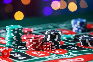 Photo of Casino chips and dice on roulette table against blurred lights, closeup