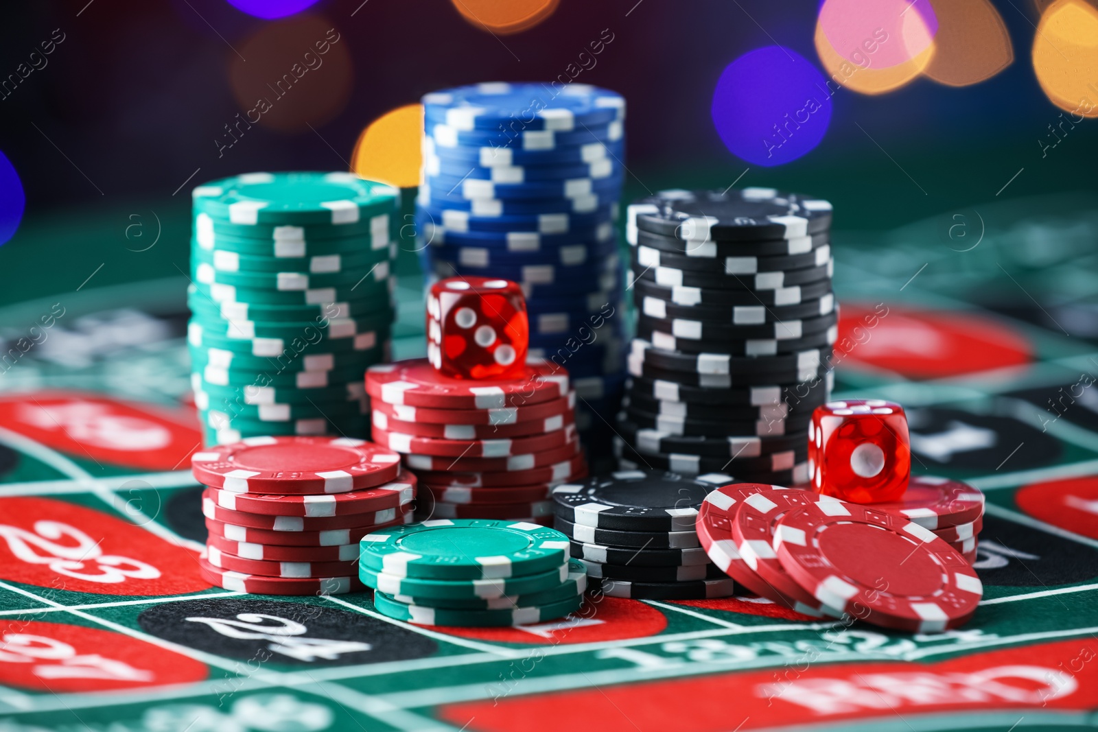 Photo of Casino chips and dice on roulette table against blurred lights, closeup