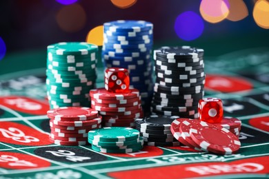 Photo of Casino chips and dice on roulette table against blurred lights, closeup